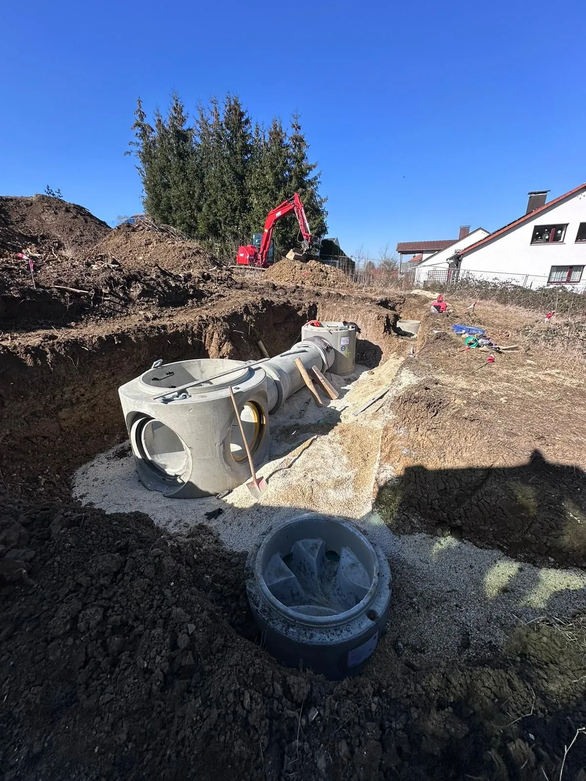Neu gesetzter Kanalschacht in der Baugrube, dahinter ein Bagger